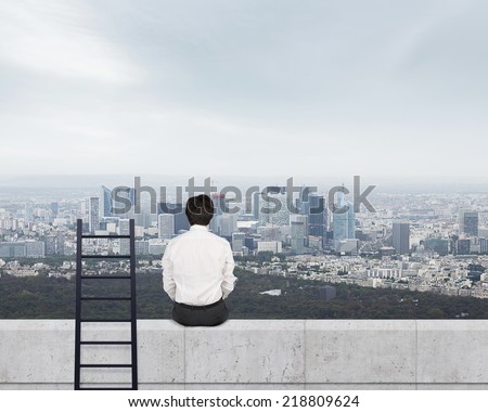 Young businessman is sitting on the edge of the skyscraper. A concept of achievement.