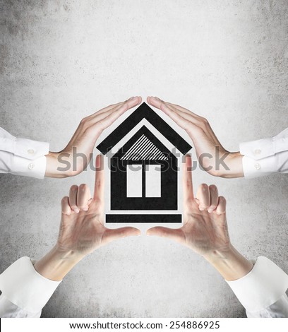 four hands holding house on gray background