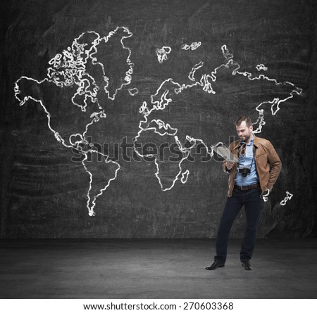 Handsome tourist is examining the map. Black wall with the sketch of the world map.