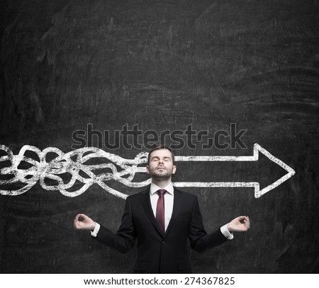 Meditative young businessman is trying to find the best solution for business development. An arrow as a symbol to the fast way of the implementation of the innovative ideas. Chalk wall background.