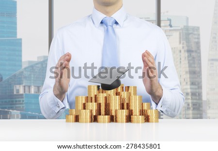 Student is placing his hands over the graduation hat and coins pyramid. A concept of a high price for the university education. New York Background.