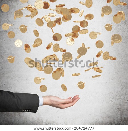 Close up of the open palm and falling golden dollar coins from the ceiling. Concrete background.