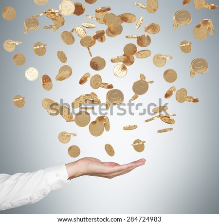 Close up of the open palm and falling golden dollar coins from the ceiling. Grey background.
