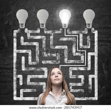 Beautiful woman is looking for the way how to solve the maze and reach the right light bulb as a concept of the perfect business solution.