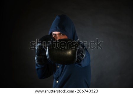 Hooded man in a fighting stance with black boxer gloves.