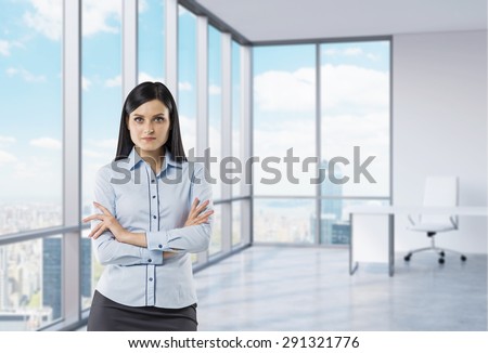 The brunette girl with crossed hands is standing in the corner panoramic office. New York view.