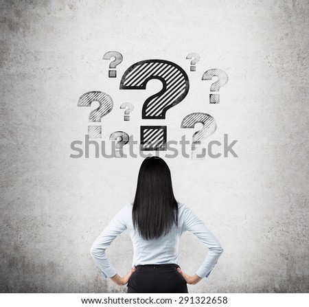 Rear view of the brunette who looks on the drawn question marks. Concrete background.