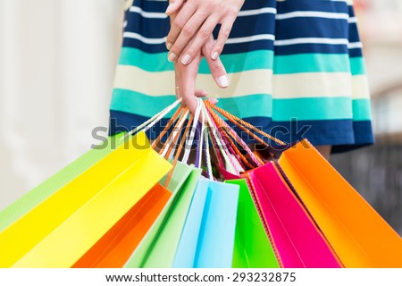 A lady in a skirt is holding a lot of colourful shopping bags.