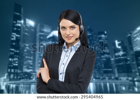 Portrait of brunette support phone operator with the headset. Business evening area of Singapore on the background.