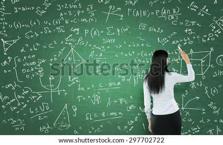 Rear view of a thoughtful woman who is writing math calculations on green chalk board.