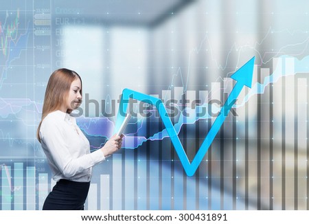 Young thoughtful lady is searching something in the internet using the tablet. Financial charts and office view in blur on the background.