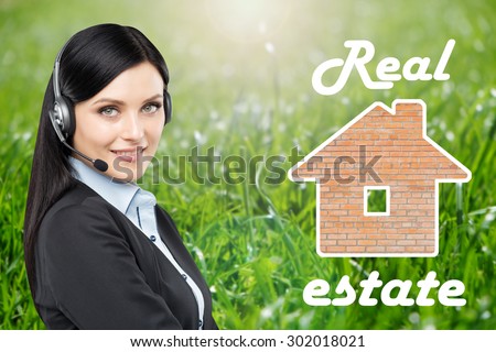 Brunette real estate agent is in a headset and a picture of the bricks house. Green grass background.
