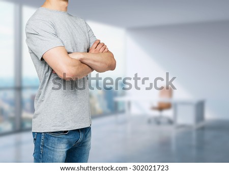 Side view of the young man in a grey t-shirt with crossed hands. Panoramic office view in blur.