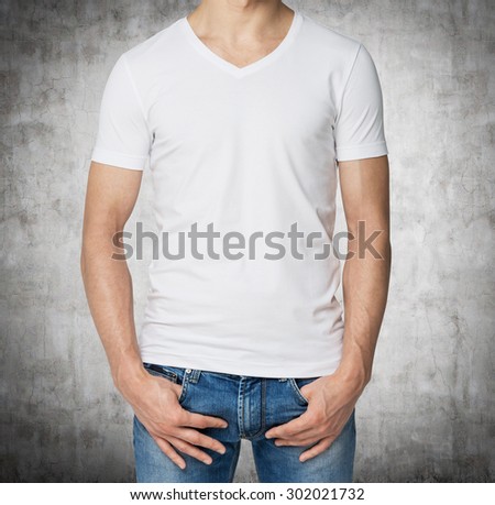 Young man in a white V shape t-shirt, hands in pockets. Concrete background.