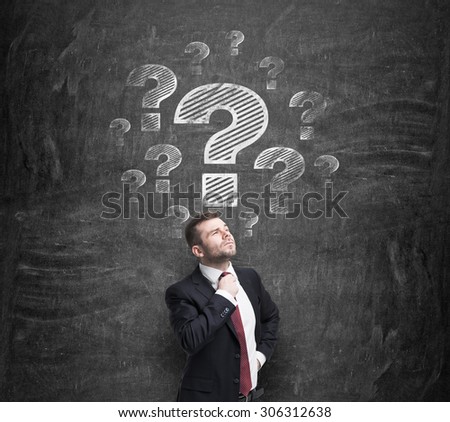 Thoughtful businessman is trying to find a proper solution. Question marks are drawn on the black chalkboard.
