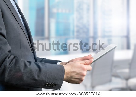 Close-up of side view of a businessman who is browsing on his tablet. Office view with Singapore panoramic view.