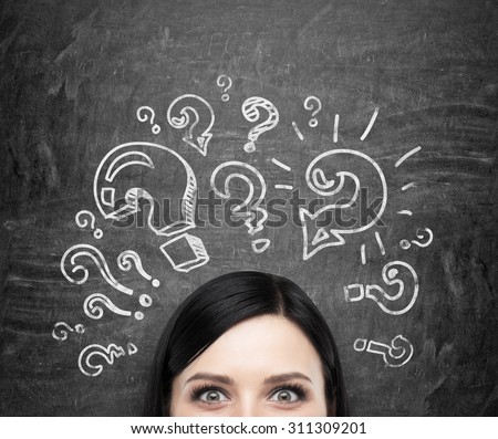 A forehead of the brunette girl who is pondering about unsolved problems. Question marks are drawn around the head. black chalkboard background.