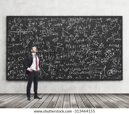 Side view of a confident young man who stands in front of black chalkboard which is full of math formulas. A concept of Analyst at investment bank.
