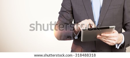 A man in formal suit is looking for some data in the tablet. Light on the background is similar to the sunset.