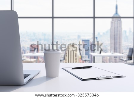 A workplace in a modern panoramic office in Manhattan, New York City. A laptop, notepad and a coffee cup are on the white table. 3D rendering.