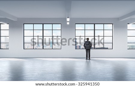 Full length a man in formal suit who is looking out the window in New York, modern loft style open space.