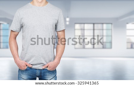 Front view of a man in a light grey t-shirt and denims. Modern loft style open space on the background.