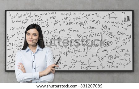 A beautiful brunette is pondering about the solution of complicated analytical problem. Math formulas are written down on the whiteboard. Concrete wall.