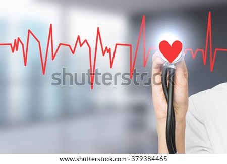 A hand listening to a red heart with a phonendoscope, the heart is a part of a cardiogram. Blurred office background. Concept of medical examination.