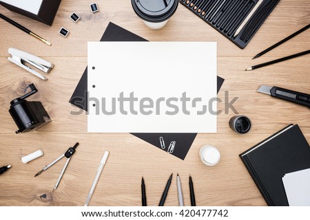 Top view of blank white paper sheet, black stationery items, several drawing tools and coffee cup. Mock up