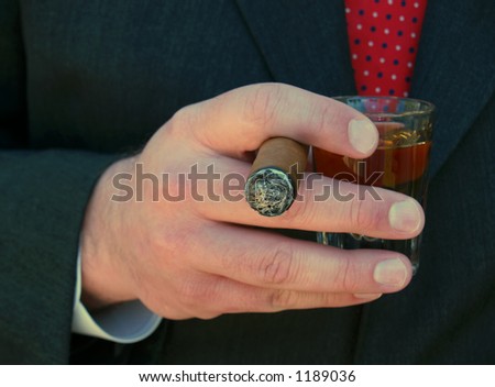 man in suit smoking a cigar and holding a shot of whiskey
