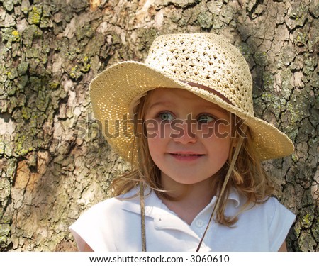little girl in big straw sun hat leaning against tree bark
