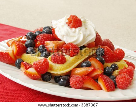 breakfast of waffles on a plate with mixed berries and whipped cream