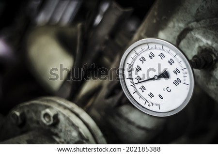 Industrial temperature gauge with out of focus pipes in background