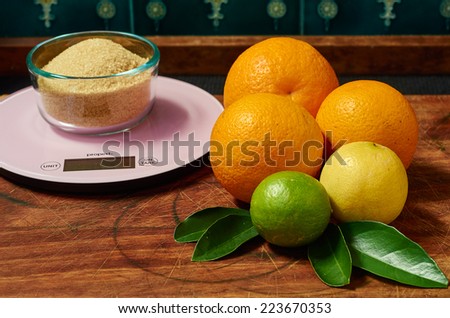 Three oranges, a lime and a lemon on a wooden board with brown sugar on a scale in preparation for making marmalade.