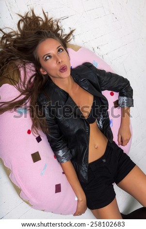 Young woman fooling around and showing tongue on the big donut. White brick wall not isolated