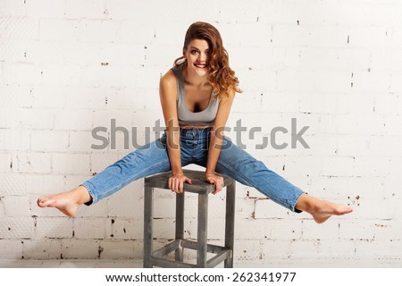 Smiling young woman doing acrobatics on a chair. White brick wall not isolated