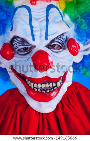 Scary clown person in clown mask on blue background studio shot