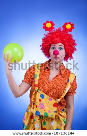 Sad clown with a ball in hands on blue background. Studio professional lighting
