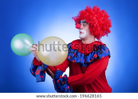 Clown with two balloons in hand on blue background. Studio professional lighting