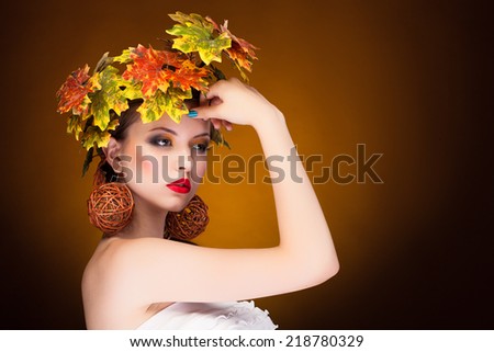 Fashion autumn concept of young woman on brown yellow background. Fashion art and glamour autumn concept. Fall. Leaves in head