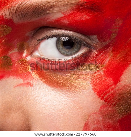 Close up shot of an eye with painted face. Red and gold tones. Perfect clean skin. Stage make up. Vivid colors