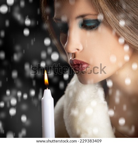 Sensual woman blowing candle in snow. Studio shooting. Winter theme. Merry Christimas. Woman is dressed in luxury white fur