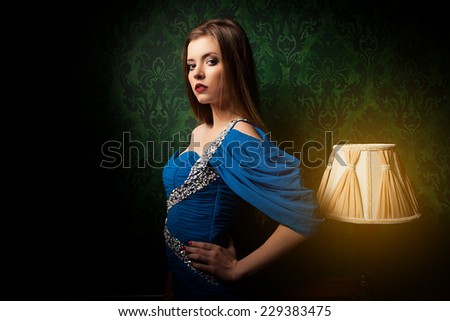 Beautiful girl in vintage room next to a lamp. Rich retro green interior. Old lamp next to the girl. Sensuality and luxury. Fine art