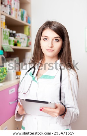 Young pharmacist with digital tablet in hands next to druggs and pills storage. Health care business. Young specialist