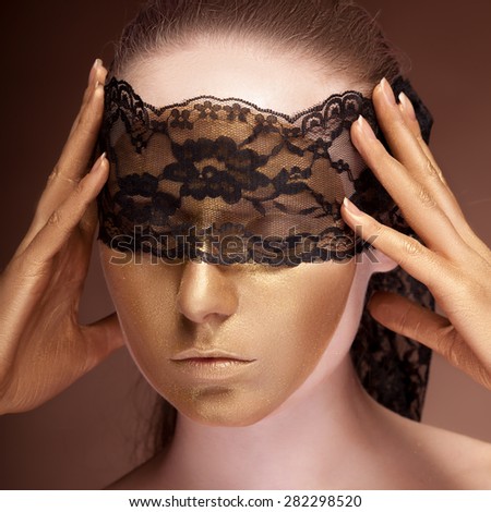 Sensual woman with a lace on her face. Gold skin make up. Fashion gold make up