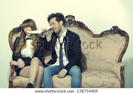 Boy playing with his girlfriend sitting on the couch with a feather old