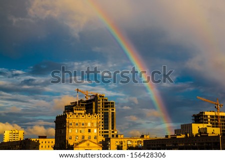 Photo of bright colorful rainbow over city, sun shining in rainy day, beautiful colors phenomenon in dark blue sky, overcast weather, nature landscape in the town, autumn, gh