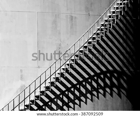 Heavy shadow of stairway on old white storage tank. Stairs cast interesting shadows in the late afternoon Sunlight. Black and White
