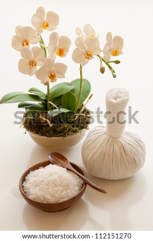 Exfoliation salt scrub, herbal massage ball and white orchids in a vase.