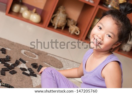 Cheerful girl playing  with domino game, sitting on floor.